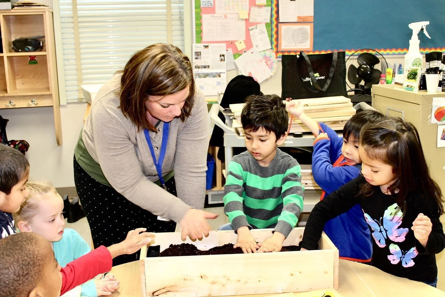 A teacher and her kindergarten class filling a new garden box with soil