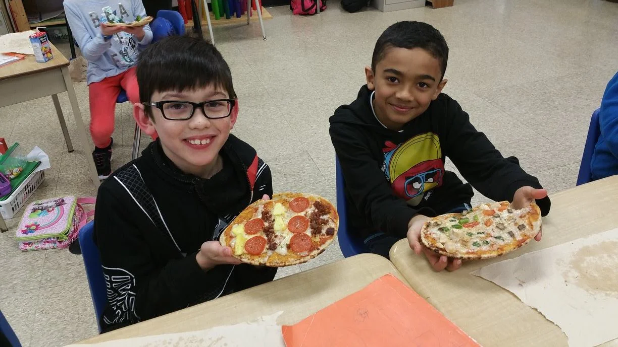 Classmates, including Brian Renaud, proudly holding up pattern pizzas topped with beet greens grown in their classroom garden