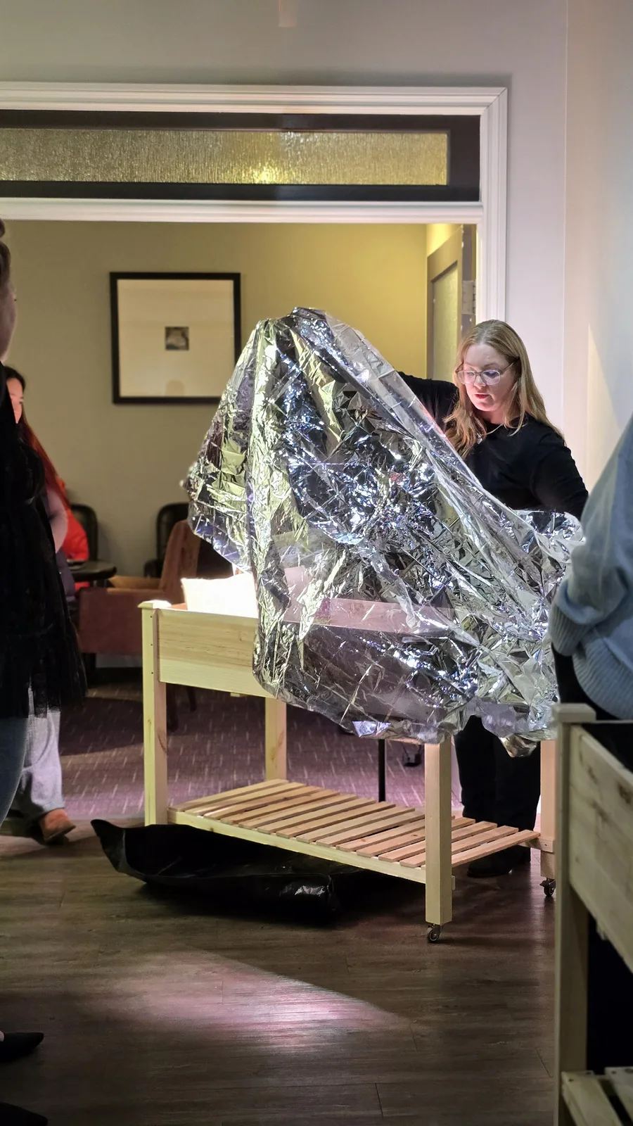 A teacher covers a Junior Green Thumbs classroom garden with a thermal blanket over the holidays, creating a mini greenhouse for a lesson on osmosis and condensation