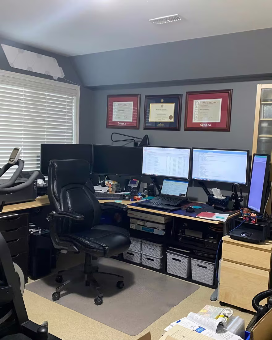 Busy home office with three monitors, a desk and storage boxes, before staging