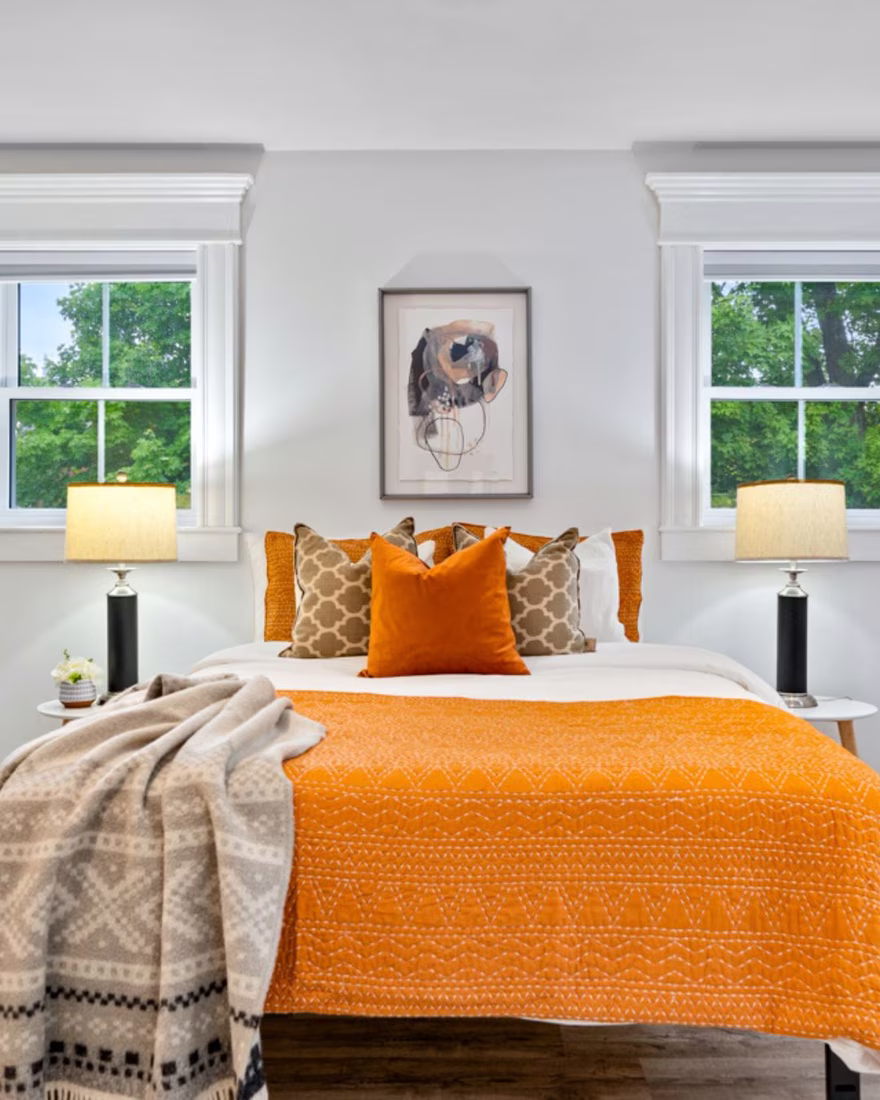 Primary bedroom after staging, with warm orange bedding, layered pillows and natural light